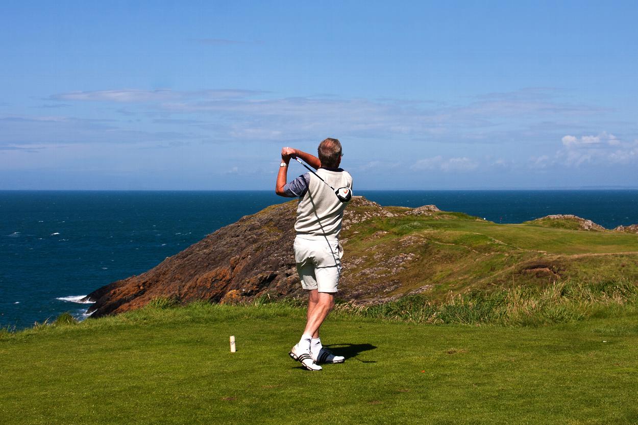 Golfer swinging club on Welsh coast